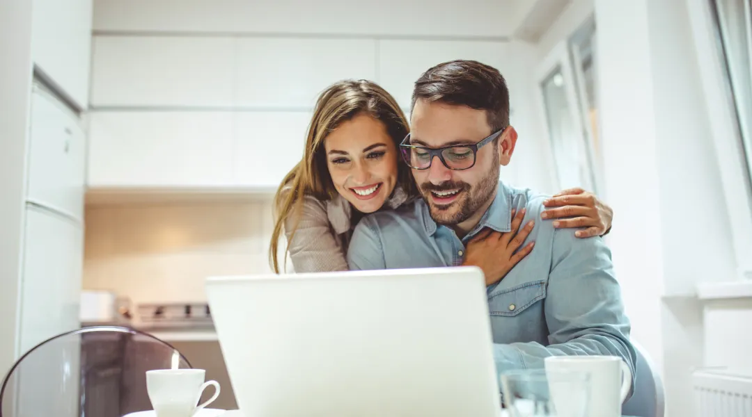 Un homme et une femme sourient en regardant un ordinateur portable sur un canapé. Cote de crédit.