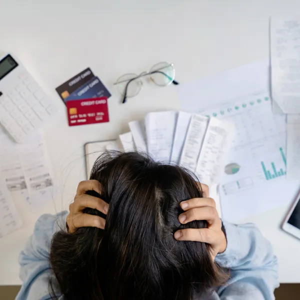 Femme stressée tenant sa tête dans ses mains, entourée de factures sur son bureau. Cote de crédit.